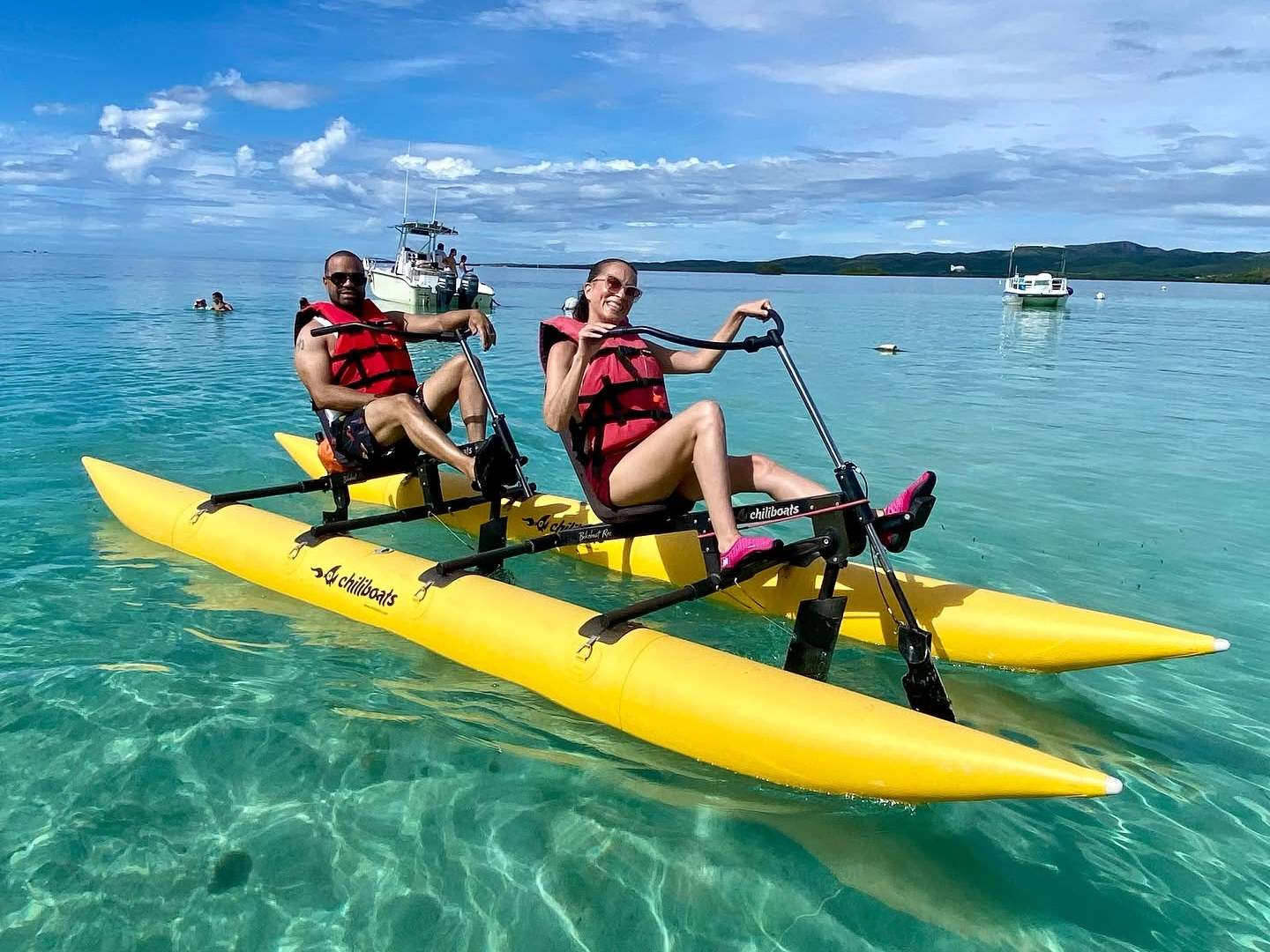 Two people pedal kayaking on clear turquoise water under a blue sky.
