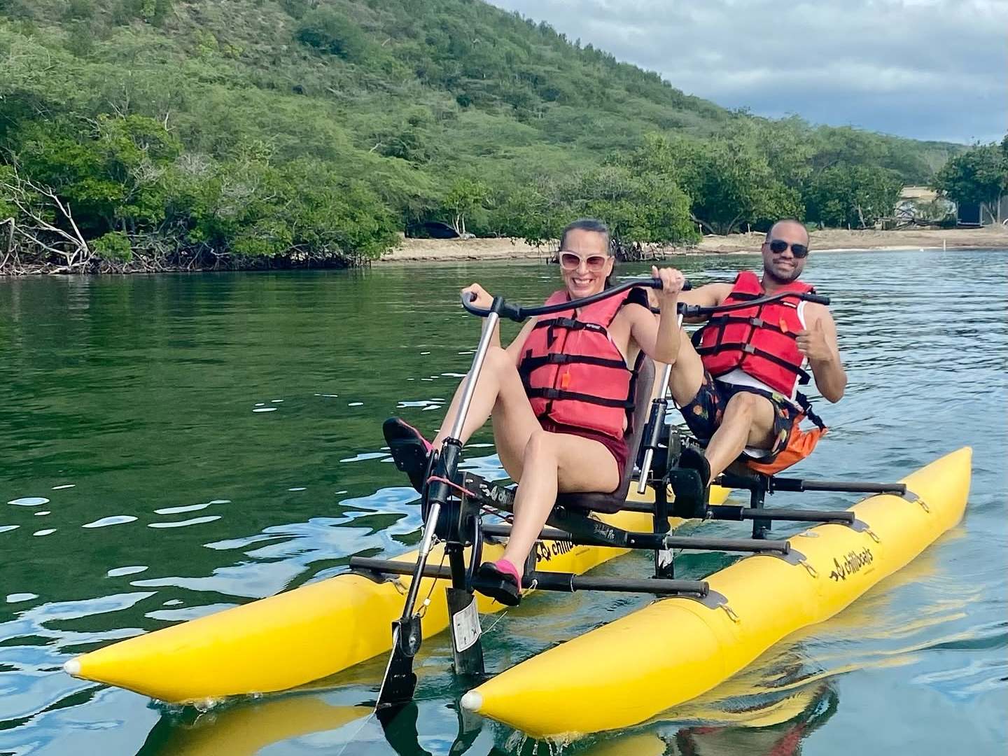 Two people smiling, paddling a yellow water bike on a lake.