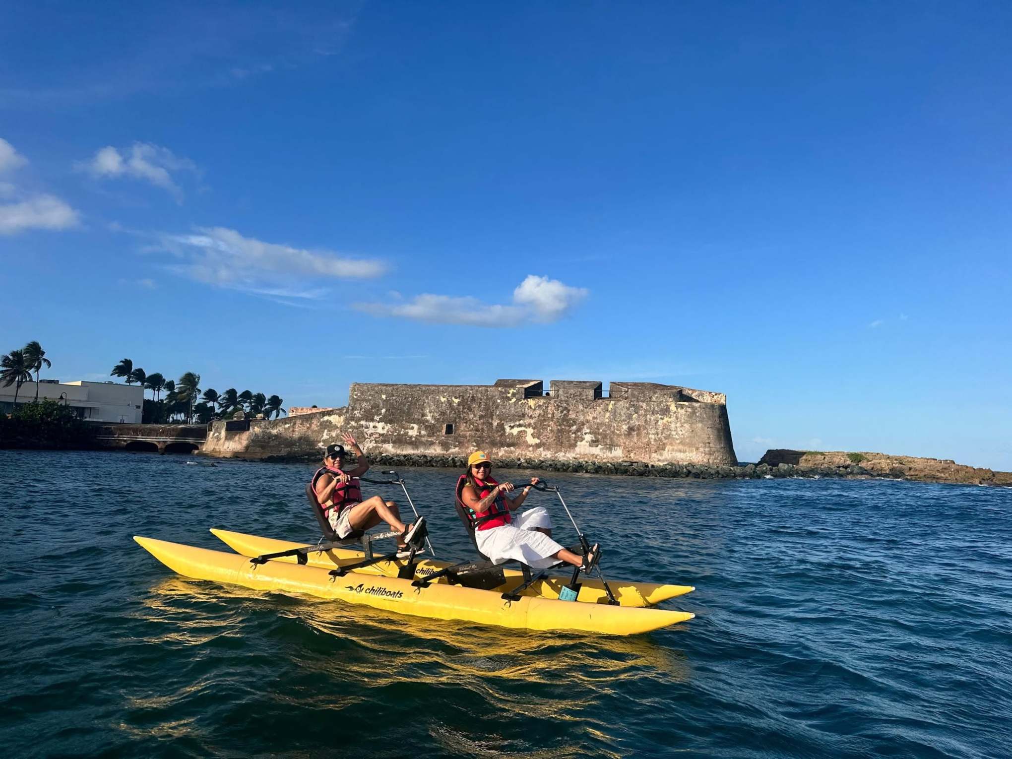 Two people on a yellow water bike near a historic stone fort in clear weather.