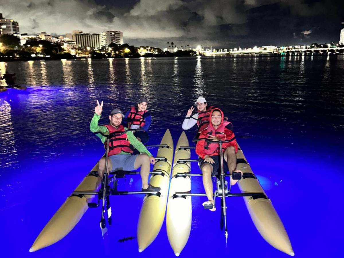 Three people on illuminated water bikes at night with city lights in the background.