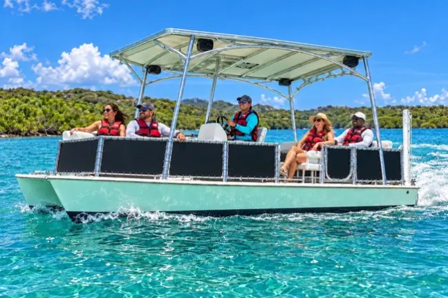Six people in life jackets on a canopy-covered boat in clear blue waters.
