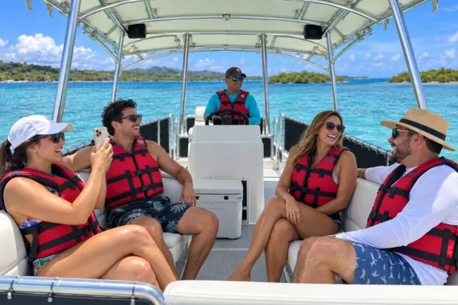 Group of people wearing life jackets on a boat, smiling and enjoying a sunny day on the water.
