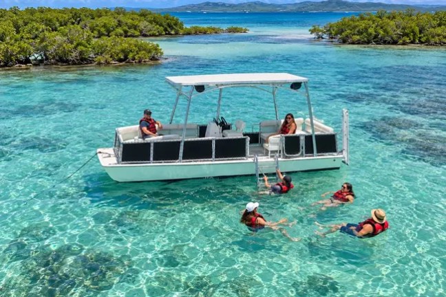 People swimming near a boat in clear blue water surrounded by small islands.