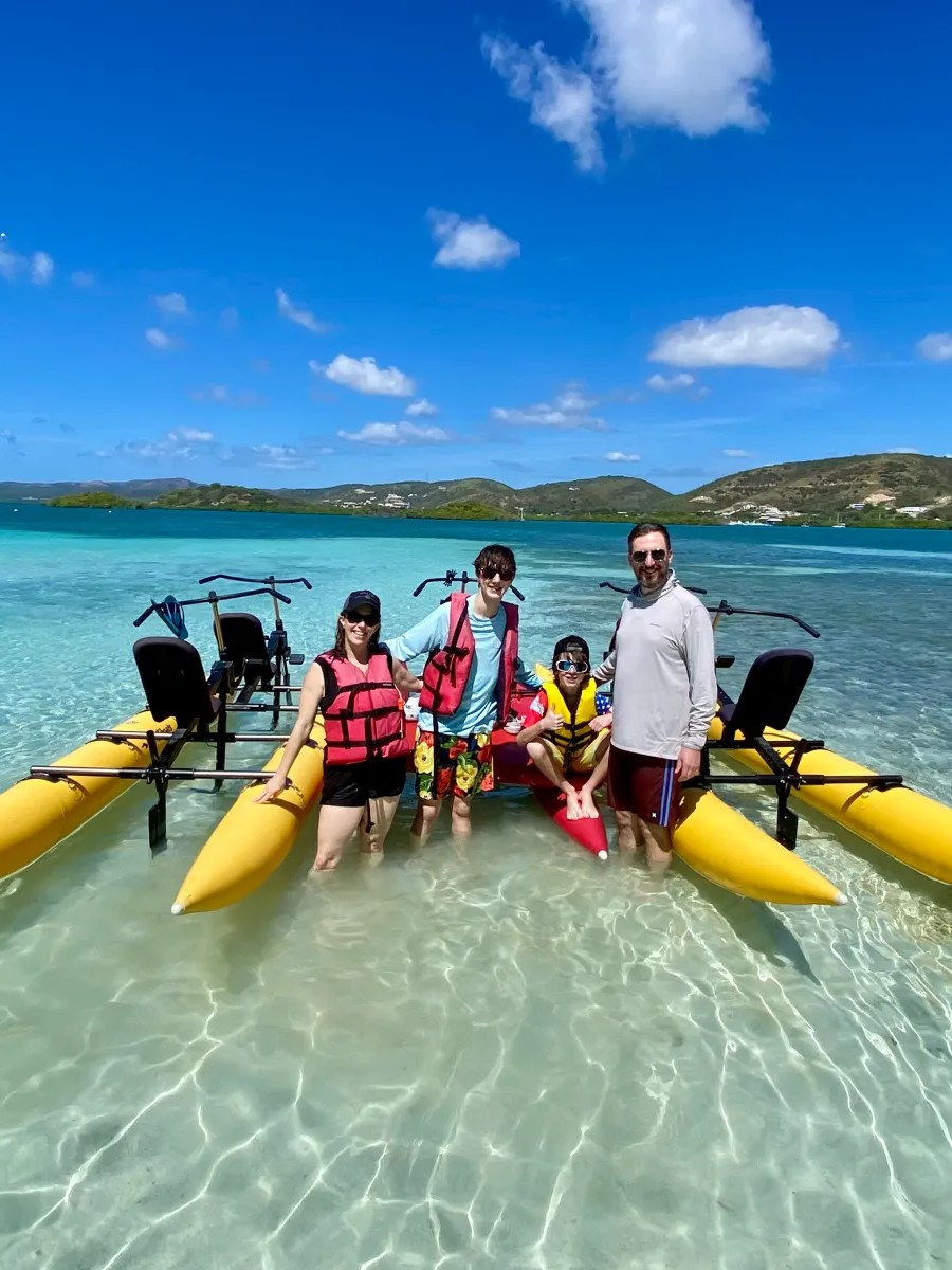 Four people with yellow watercrafts in shallow, clear ocean.