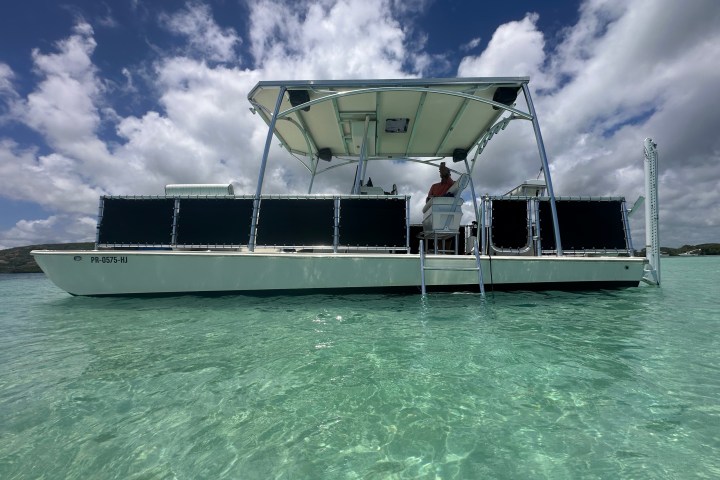 Pontoon boat on clear turquoise water under a cloudy sky.