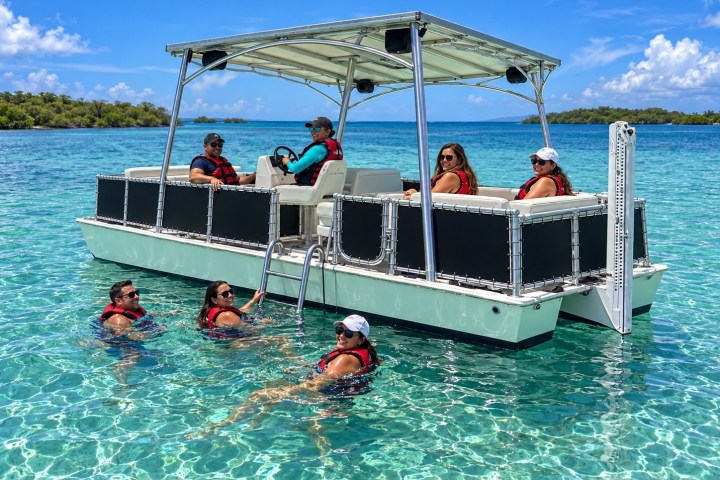 People in life vests on a boat and swimming in clear blue water.