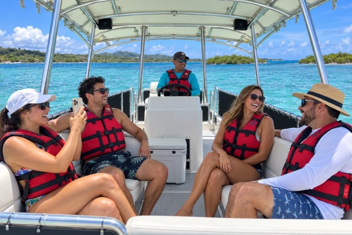 Group of people on a boat in life jackets, enjoying a sunny day on the water.