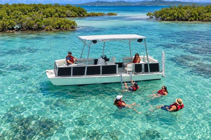 Group swimming near a boat in clear turquoise water with lush islets.